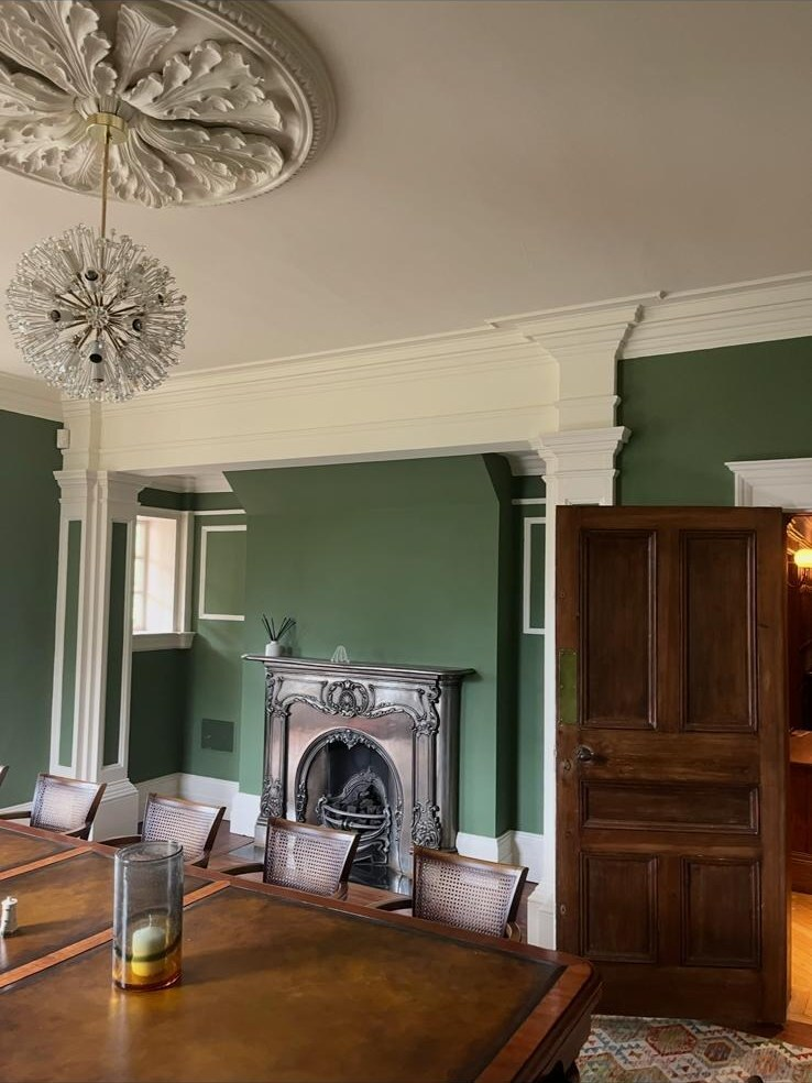 Green dining room with ornate cornicing, fireplace and careful decorating work