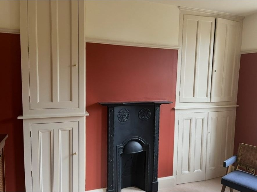 Terracotta feature wall with hand-painted cream fitted joinery flanking a cast-iron fireplace